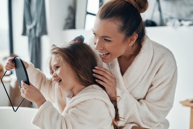 Beautiful young mother combining her daughter?s hair while doing morning routine