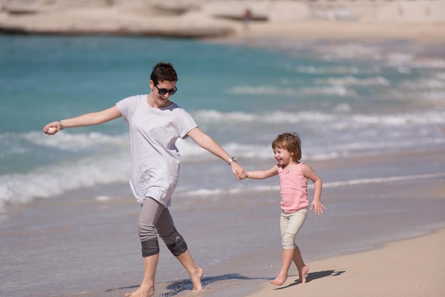 La bella giovane madre e la bambina sveglia si divertono mentre corrono su una spiaggia esotica lungo l'oceano viaggi e vacanze.