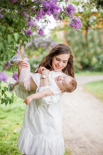 Beautiful young mother and daughter near the blossoming lilac. Spring.