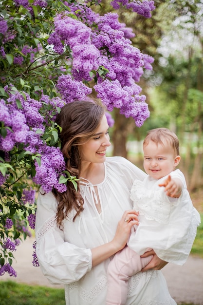 Beautiful young mother and daughter near the blossoming lilac. Spring.