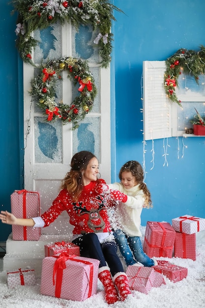 Beautiful young mother and daughter sitting near red holiday boxes tied with ribbon