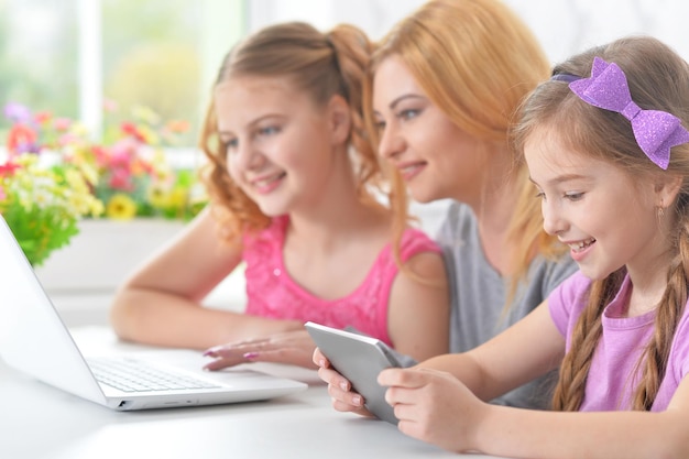 Beautiful  young mother  and  girls sitting at  table and using  laptop