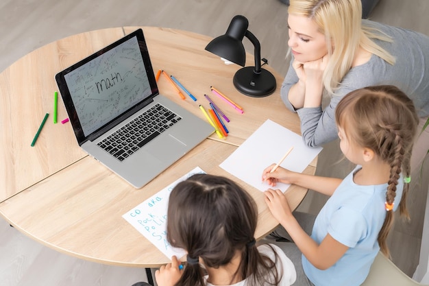 Beautiful young mother helping her daughters with homework.