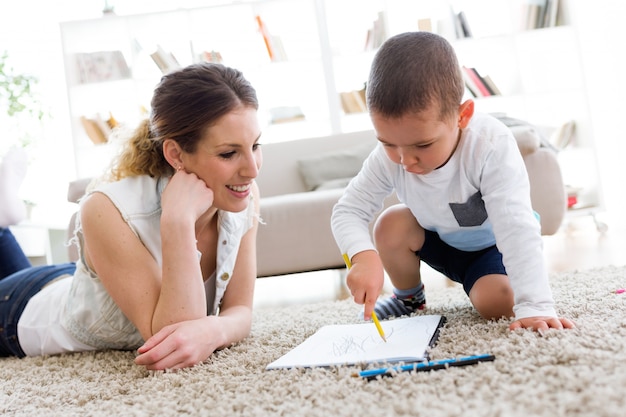 Beautiful young mother and her son drawing at home.