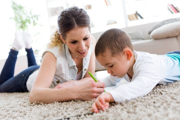 Beautiful young mother and her son drawing at home.