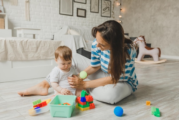 Beautiful young mother plays and teaches her baby 6 months old on the floor in the living roommom and baby play with toys