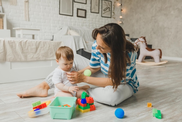 Beautiful young mother plays and teaches her baby 6 months old on the floor in the living roommom and baby play with toys