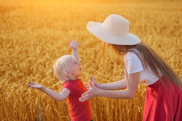 美しい若い母親が田園地帯で小麦畑の休日に息子と遊ぶ