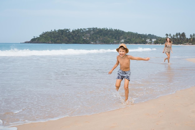 Beautiful young mother and son run at beach in sunny day and hugging