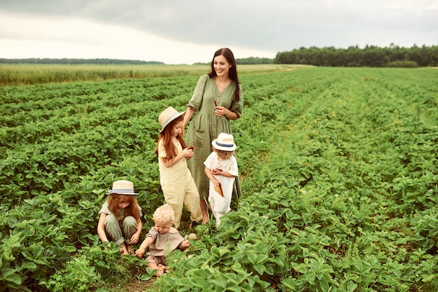 Beautiful young mother with children in a linen dress with a basket of strawberries gathers a new crop and has fun with the children