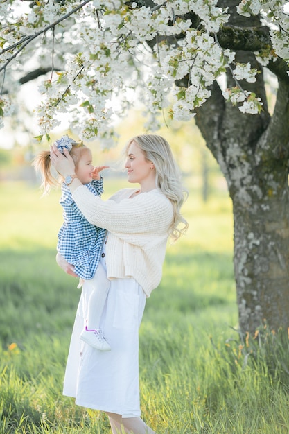 A beautiful young mother with her little daughter are resting on a picnic in the flowering garden