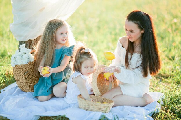 Beautiful young mother with little daughters on a picnic in the field Summer breakfast with lemons