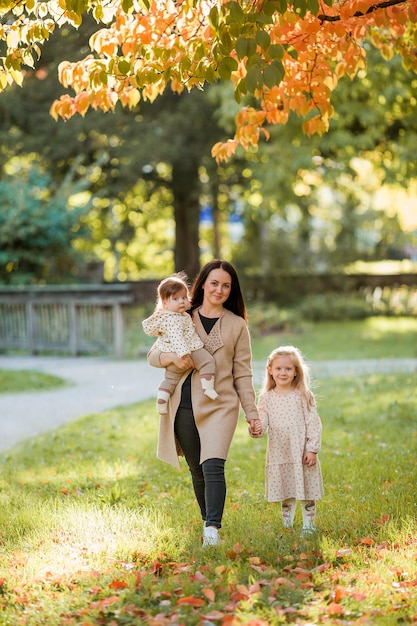 Beautiful young mother with two small children walks in the autumn park Portrait of a happy family Fall