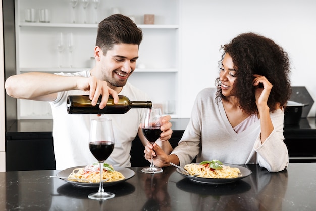 집에서 낭만적 인 저녁 식사를하고, 레드 와인을 마시고 파스타를 먹고, 쏟아지는 아름다운 젊은 다민족 부부