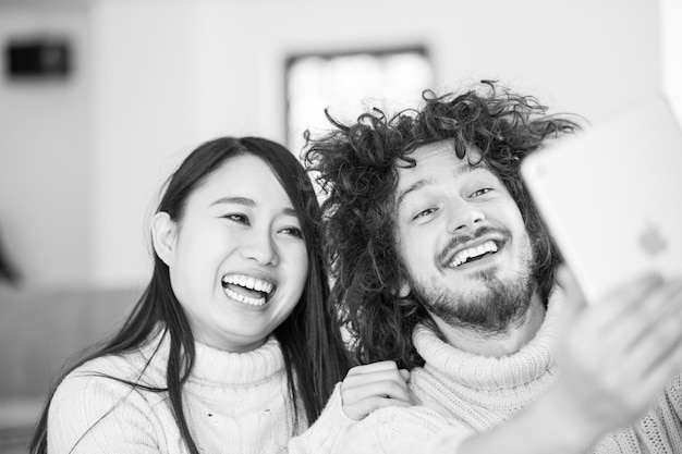 beautiful young multiethnic couple using tablet computer in front of fireplace on cold winter day at home