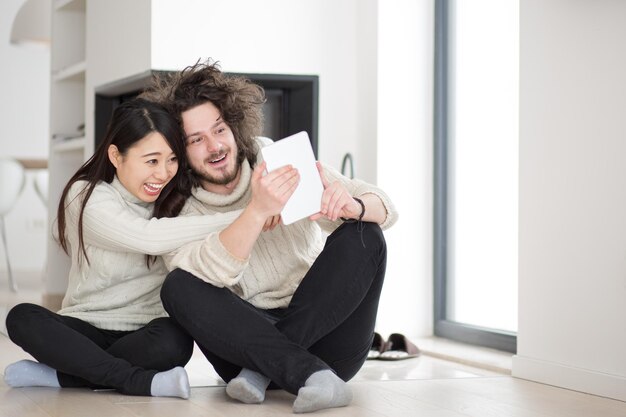 beautiful young multiethnic couple using tablet computer in front of fireplace on cold winter day at home