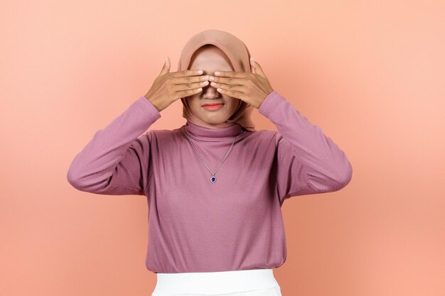 Beautiful young muslim woman covers her eyes with her hands feels embarrassed afraid and doesn't want to see wearing purple sweater