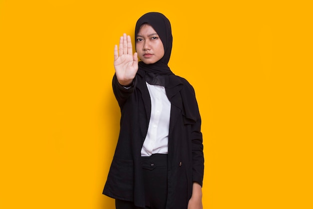 beautiful young muslim woman hand doing stop sign with serious expression defense gesture on yellow