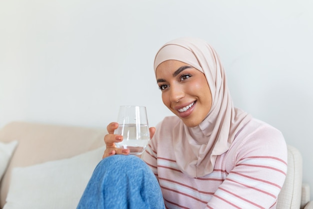 Bella giovane donna musulmana con l'hijab che beve un bicchiere d'acqua fresca a casa