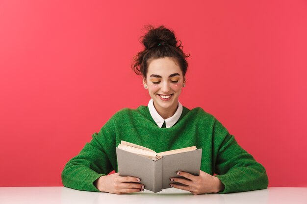 Beautiful young nerd student girl sitting at the table isolated, studying with books,