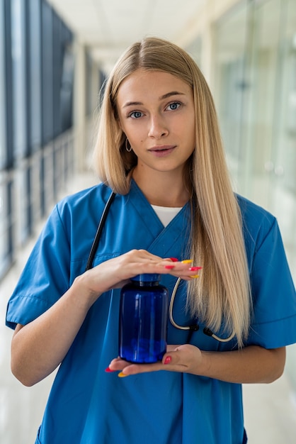 Bella giovane infermiera in uniforme che tiene una bottiglia blu con la medicina nelle sue mani in ospedale. concetto di medicina