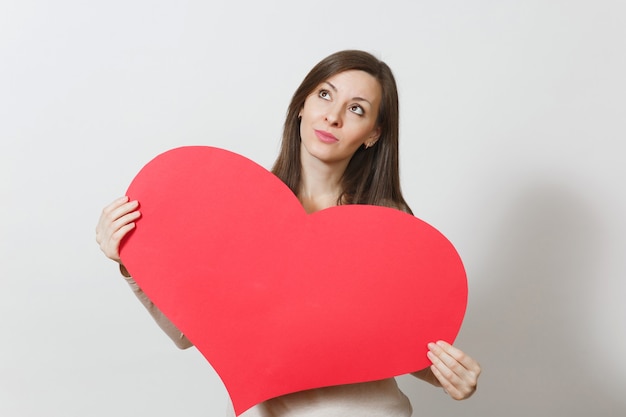 Beautiful young pensive woman holding big red heart in hands isolated on white background. Copy space for advertisement. With place for text. St. Valentine's Day or International Women's Day concept.