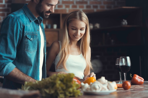 Foto i bei giovani parlano e sorridono mentre cucinano cibo sano in cucina a casa