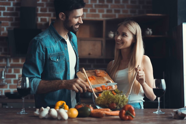 Beautiful young people are talking and smiling while cooking healthy food in kitchen at home