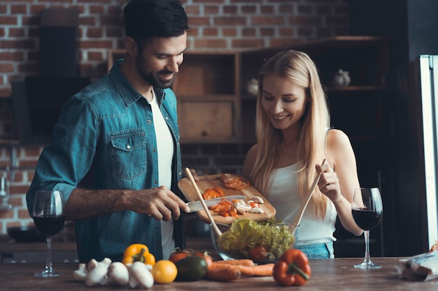 Beautiful young people are talking and smiling while cooking healthy food in kitchen at home