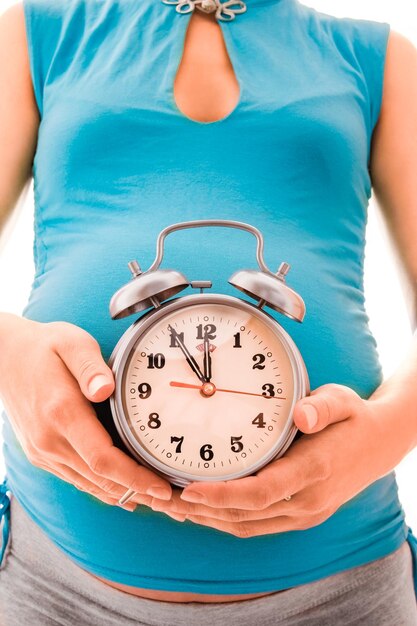 Beautiful young pregnant girl on a white background with alarm clock