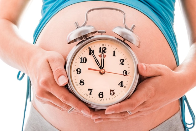 Beautiful young pregnant girl on a white background with alarm clock