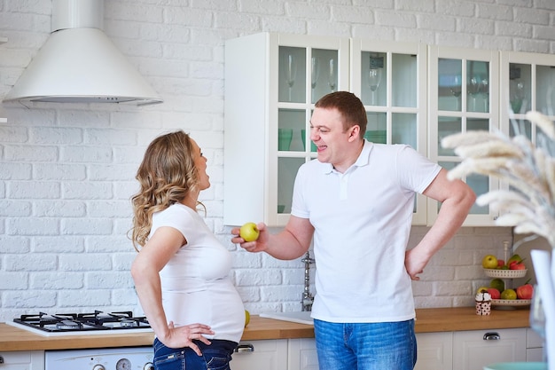 Beautiful young pregnant girl with her husband laughing in the kitchen in a beautiful interior.