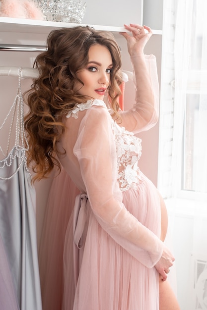 Beautiful young pregnant lady in a pink dress at home