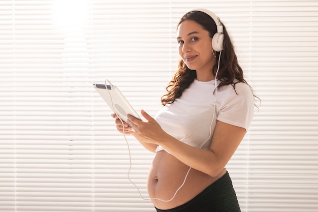 Beautiful young pregnant woman chooses music by subscription and listens to it through headphones