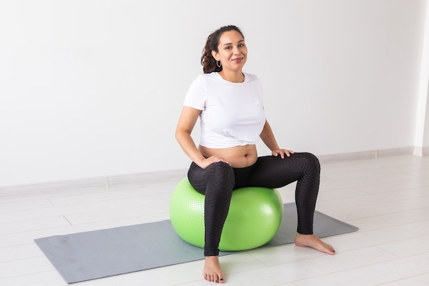 Beautiful young pregnant woman doing exercise at home on fitball.