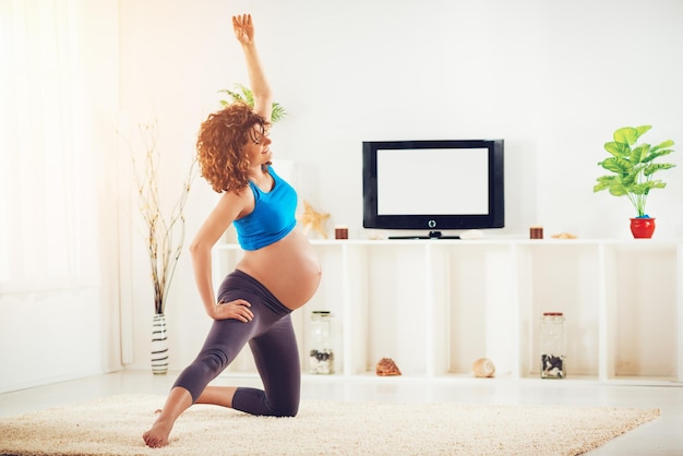 Beautiful young pregnant woman doing exercises at the home.