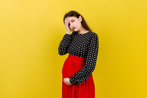 Bella giovane donna incinta che sente mal di testa su sfondo colorato isolato donna incinta o problemi della madre stressati