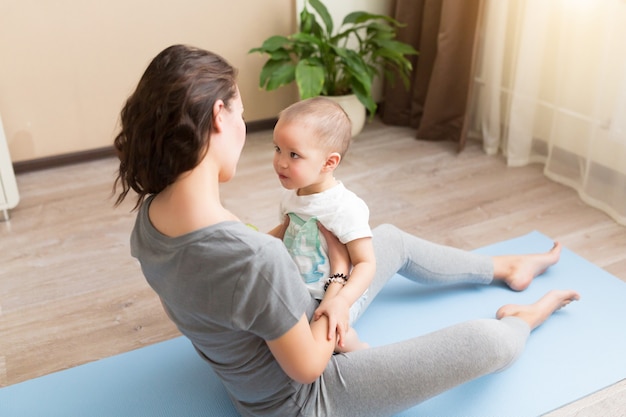 Beautiful young pregnant woman and little kid boy smiling while lying on yoga mat