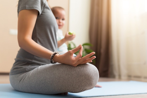 Beautiful young pregnant woman and little kid boy smiling while lying on yoga mat