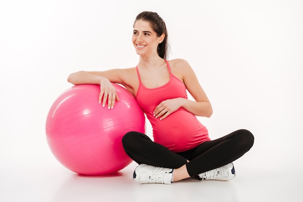 Beautiful young pregnant woman sitting with fitball and looking away