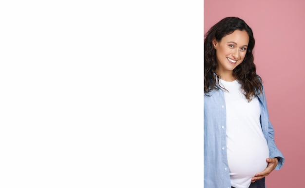 beautiful young pregnant woman standing by white blank board