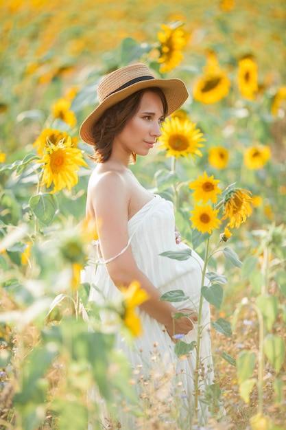 ひまわり畑の美しい若い妊婦。太陽の下で若い妊婦の肖像画。夏。