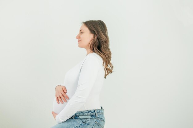 Photo beautiful young pregnant woman on white background stylish model with belly in a white bodysuit