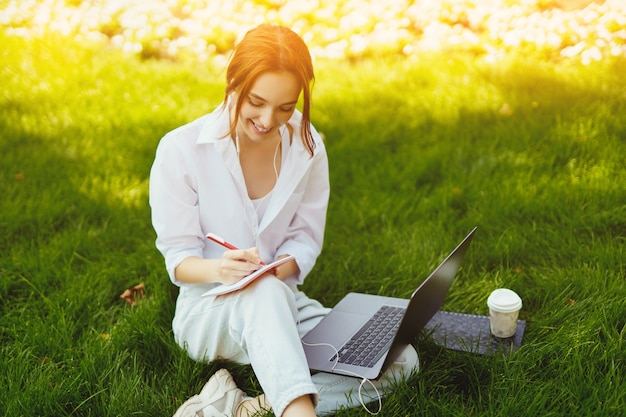 Beautiful young pretty redhead woman in park outdoors using laptop computer for study or work wired ...