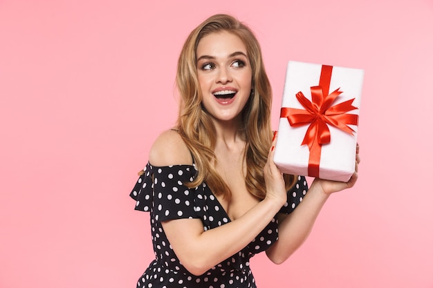 A beautiful young pretty woman posing isolated over pink wall holding present gift box