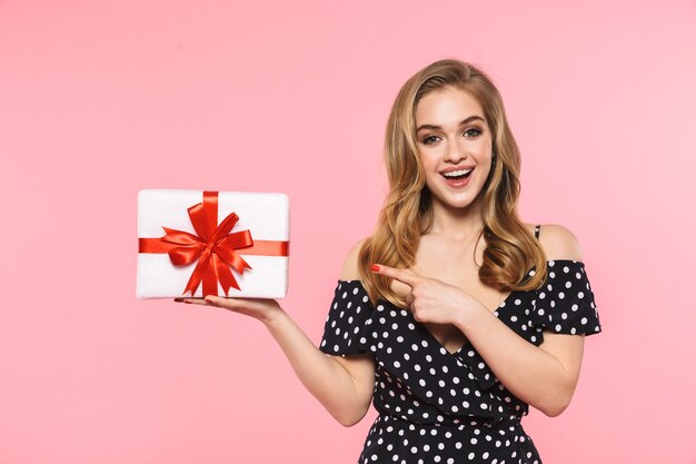 a beautiful young pretty woman posing isolated over pink wall holding present gift box