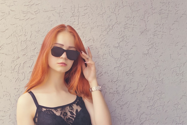 Beautiful young red hair woman in sunglasses on textured concrete