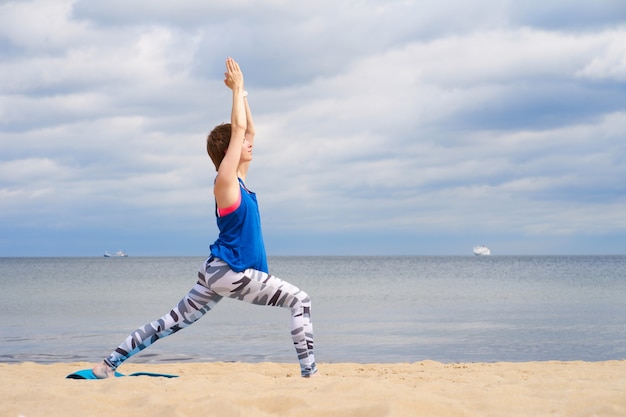 Photo beautiful young redhead woman practicing yoga near sea in the sunny day.