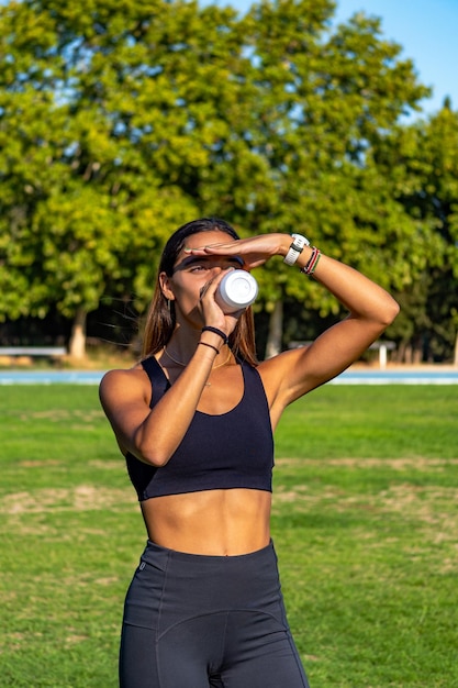 Beautiful young runner tanned protecting her eyes from the sun with her hand looking at the horizon