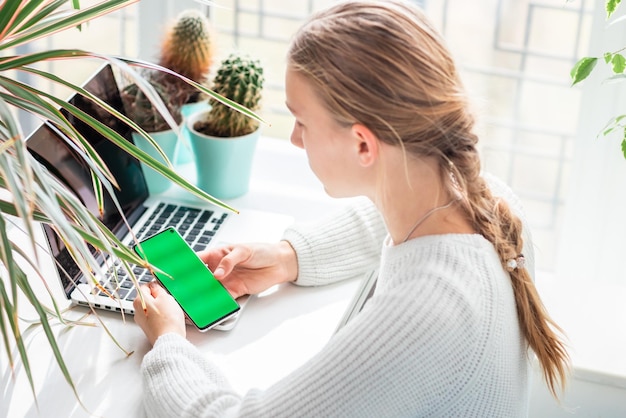 집에서 일하는 아름다운 여학생이 크로마키 녹색 화면으로 휴대전화를 확인하고 있다